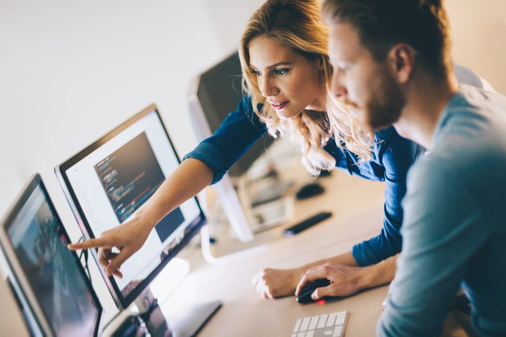 Female IT consultant explaining software data and cloud infrastructure to a male small business owner on a desktop computer