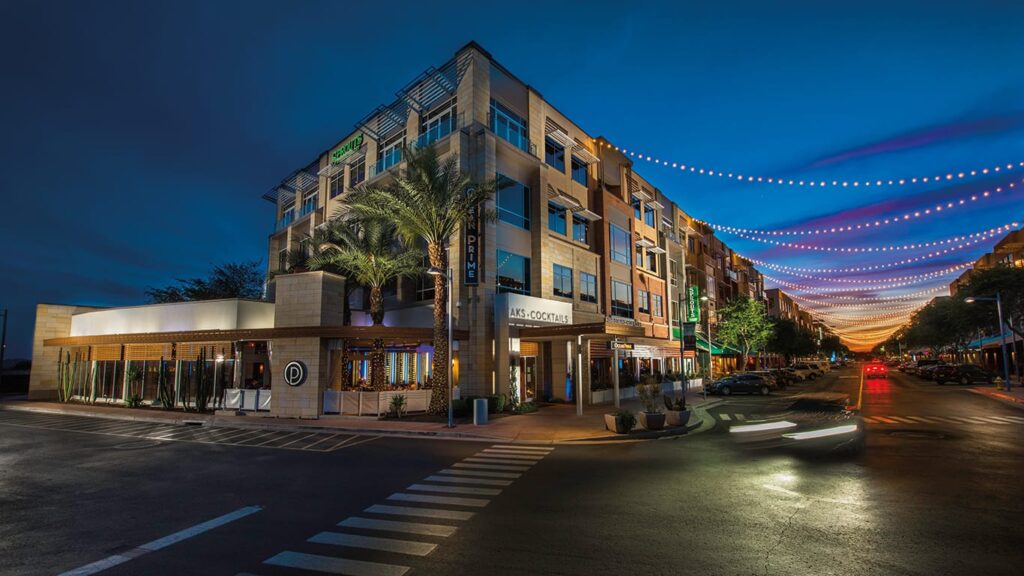 High Street commercial and dining district in North Phoenix illuminated at twilight, featuring modern architecture and pedestrian walkways.